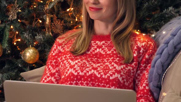 Woman with Laptop Sitting on Sofa Near New Year Tree. Christmas Celebration alt