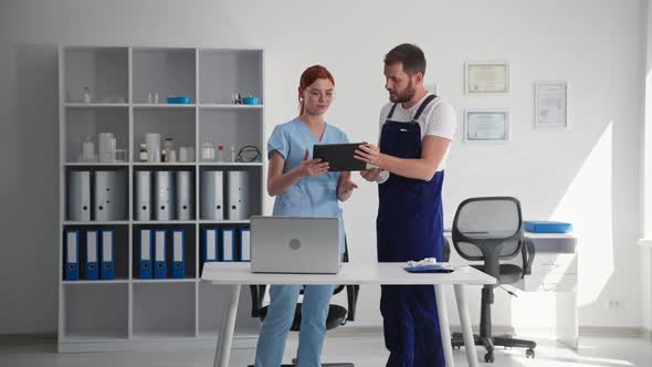 Modern Technologies Young Man Explains to Woman in Medical Clothes Work of Video Surveillance Camera alt