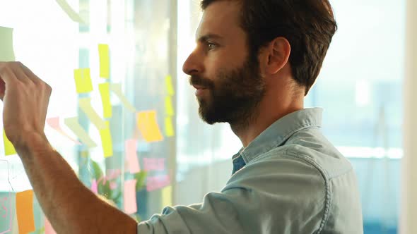 Male executive looking at sticky notes on glass alt