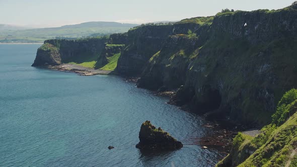 Lush Cliff Surrounded By Dark Blue Sea In Rathlin Island, Ireland With A Bird Flying On A Sunny Day  alt