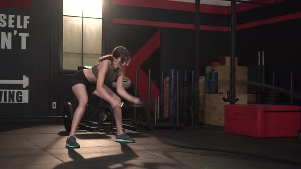 Young woman slim body training and working out with battle rope at fitness gym alt