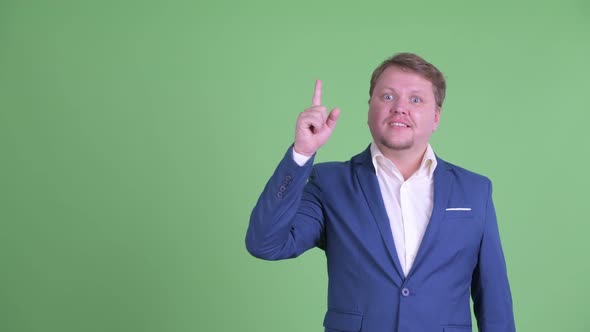 Happy Overweight Bearded Businessman Thinking While Pointing Up alt