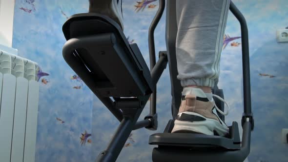 Young Girl in Sneakers is Engaged in an Orbitrek at Home Bottom View alt