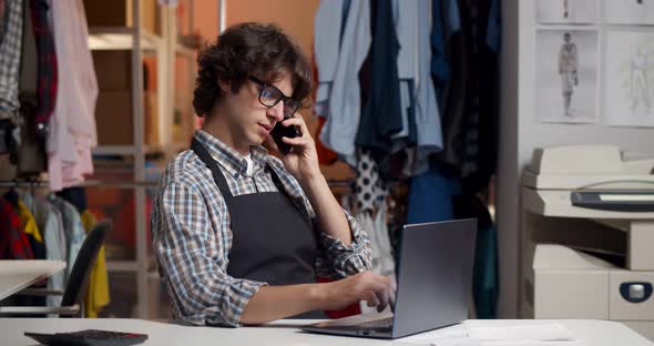Young Male Tailor Discuss Order with Client on Cellphone at Workshop alt