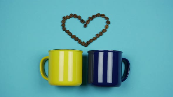 From Blue And Yellow Cups Appeare Coffee Beans Forming A Heart. Stop Motion alt