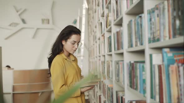 Pretty Young College Student in a Library Chooses a Book alt