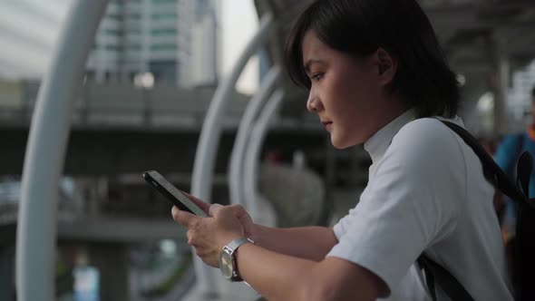 Sadness asian woman standing at the city street and use smartphone. Negative emotion