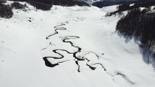 Amazing aerial view of a swirly river in the mountains during winter sunny day