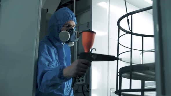 The paint engineer applies an even coat of paint to the metal frame of the future chair.