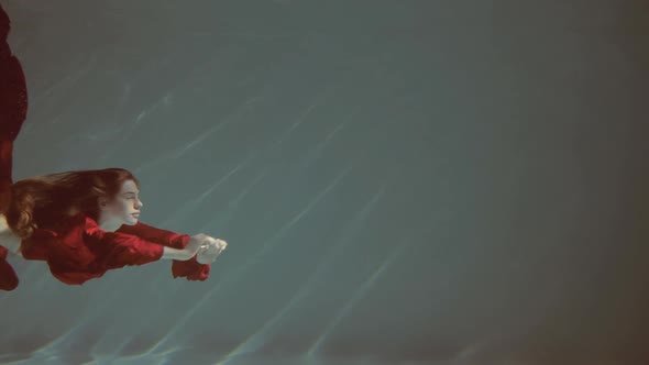 Attractive Redhaired Young Woman Swims Beautifully Underwater in a Red Dress alt