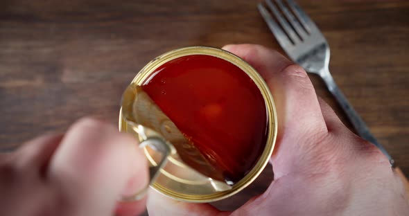 The Hands Open the Tin with Beans in Tomato Sauce. On a Wooden Background. alt
