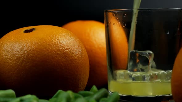 Pour Orange Juice Into A Glass And Two Oranges Next To It On Black