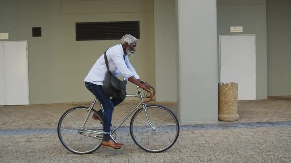 African american senior man riding a bicycle in corporate park alt