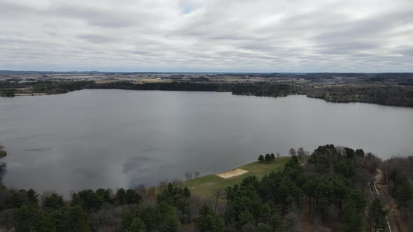 View of lake on a gray cloudy day, light ripples seen on the water surface. Small park with beach.