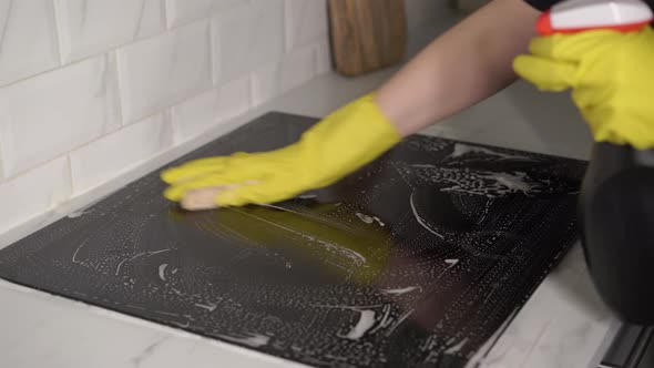 Housewife in Yellow Gloves Washes Spraying and Wipes Electric Stove at Kitchen