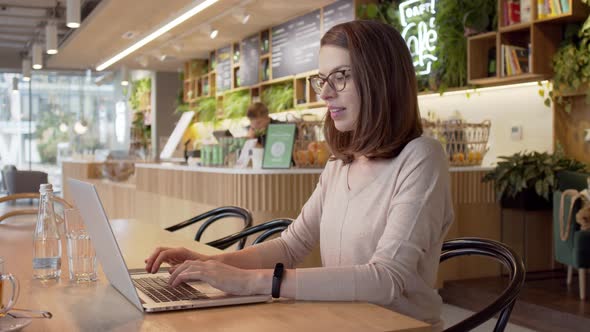 Serious Woman Attentively Looking at Monitor and Drinking Tea at Table in Cafe