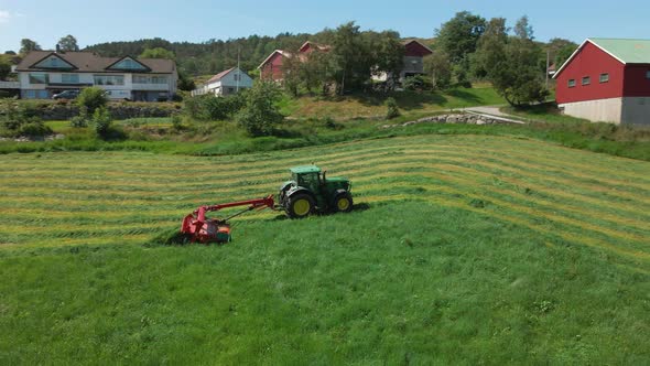 Green tractor cutting grass for hay on a farmland in Rogaland, Norway -Aerial alt