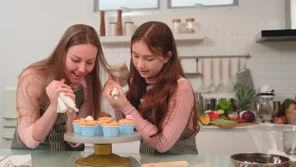 Caucasian mother and young daughter squeezes cream to decorate top of cupcake