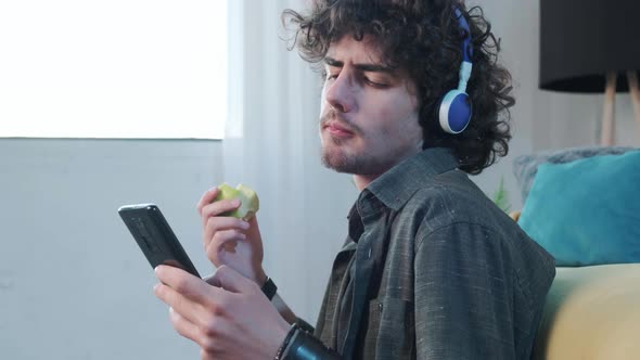 Young Man Listening to the Music and Gesturing While Eatting an Apple alt