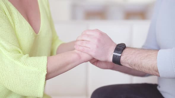 Unrecognizable Adult Man and Woman Holding Hands Sitting on Couch in Living Room alt