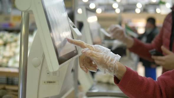 Customer in Plastic Gloves Presses Finger on Touch Screen of Electronic Balance in Supermarket alt