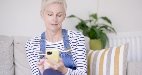 Mature woman sitting on sofa using smartphone