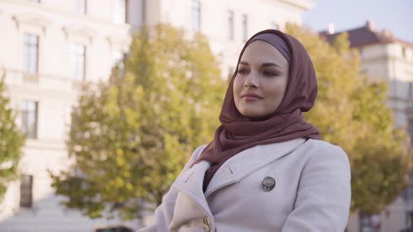 A Young Beautiful Muslim Woman Looks Around with a Smile As She Sits in a Park in an Urban Area alt