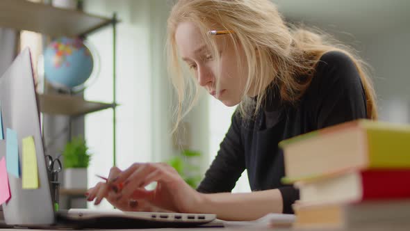 Young Blonde Woman Looking for Information on the Internet While Sitting at a Desk at Home While alt