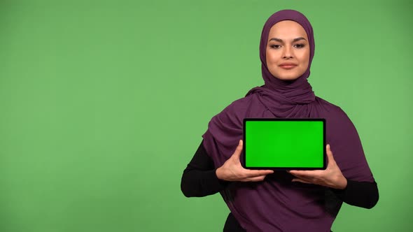 A Young Muslim Woman Shows a Tablet with Green Screen to the Camera with a Smile  Green Screen