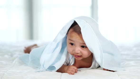 slow-motion of happy baby lying on bed under blanket in a bedroom alt