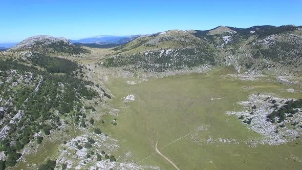 Flying above thick forest of Dinara mountain with grass plains in between alt