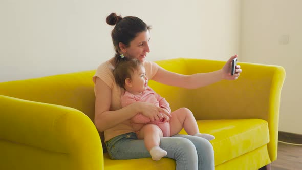 Young Happy Mother and Baby Having Video Chat with Father Using Smartphone alt