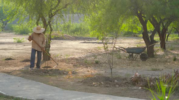 Unrecognizable Man With Hat Working In The Field And Large Garden With Worker Tool alt