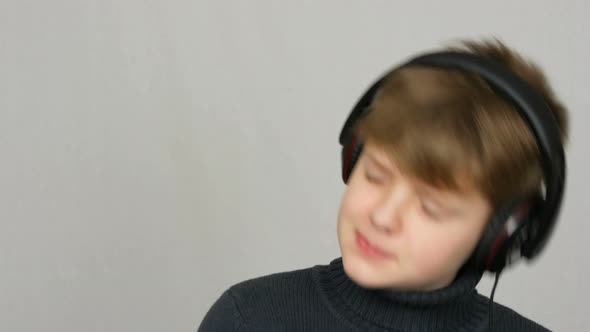 Funny Teen Boy in Big Headphones on His Head is Listening to Music Dancing and Having Fun on a White