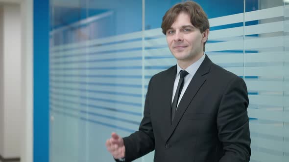Confident Elegant Young Caucasian Man Posing in Office Corridor with Documents alt