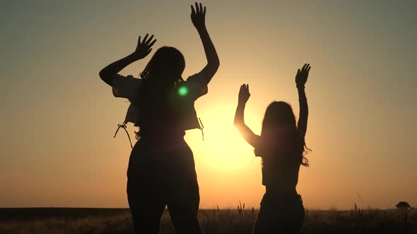 Two girls raised their hands on a field at sunset.