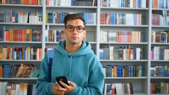 A Young Millennial Student with Glasses Flips Through the Social Network Feed on His Smartphone
