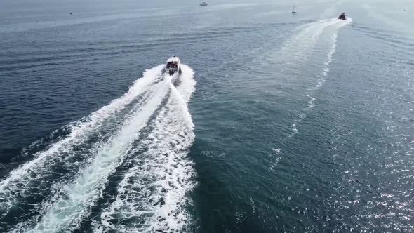 A large white boat is moving at speed on the blue sea water. alt