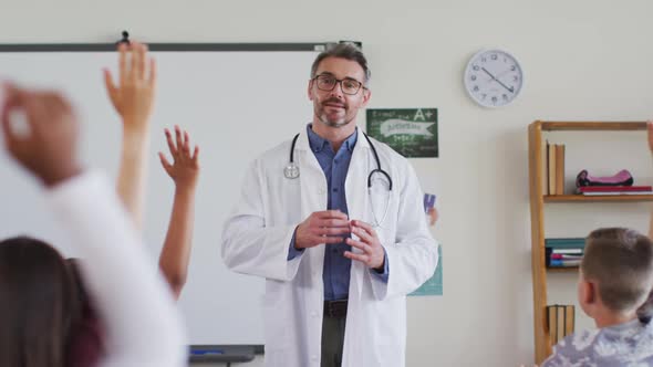 Caucasian male medical worker wearing sthetoscope, standing in classroom asking questions alt