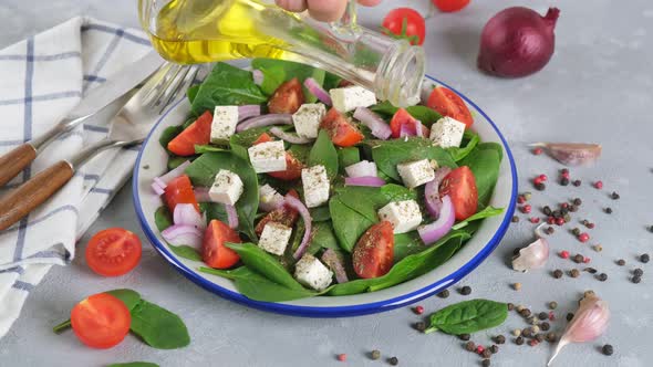 Pour olive oil on freshness salad prepared with green spinach, tomatoes, feta cheese, red onion.