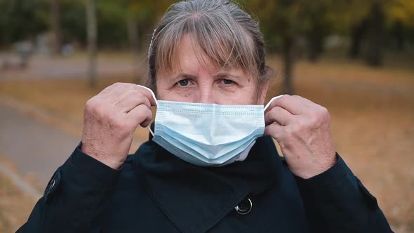 Portrait of a Senior Woman Putting on a Medical Mask and Looking Seriously at the Camera.