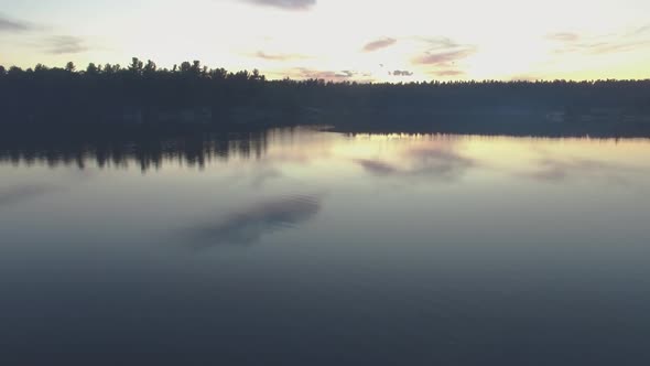 Aerial shot flying low over the still water of Charleston Lake in Ontario, Canada at sunset alt