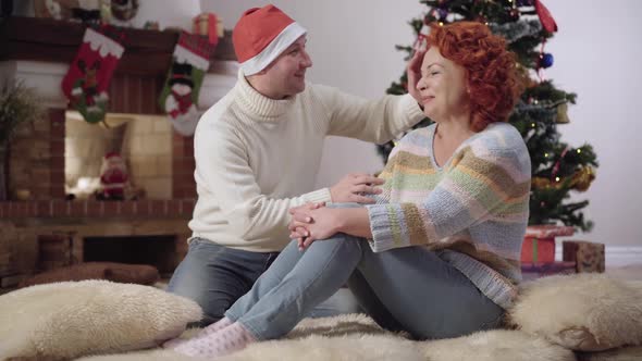 Joyful Caucasian Man Putting Christmas Hat on Head of Smiling Cheerful Woman alt