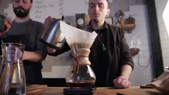 Barista pouring hot water into filter with coffee. Brewing coffee in a chemex