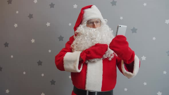 Santa Claus Using Smartphone Taking Selfie Posing Wearing Red Costume and Hat alt