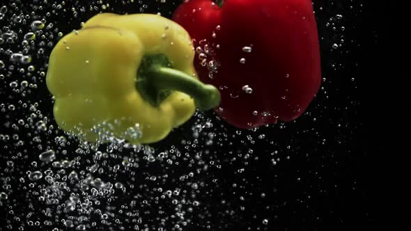 Ripe Fresh Bell Peppers Falling Into Water on Black Background alt