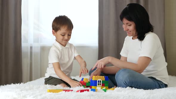 Happy Family: Mother and Son Play Building a House of Colored Blocks. The Child and Mother Play alt