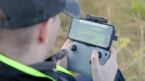 Drone Operator Hands Using Remote Control with Sticks and Cellphone As Monitor at Daylight