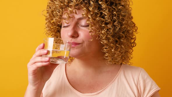 Happy Optimistic Young Woman Holding a Glass of Water to Drink Over Yellow Background Very Happy and