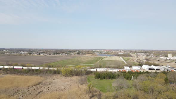 Drone view with open farm field, train tracks, retention pond and blue sky.